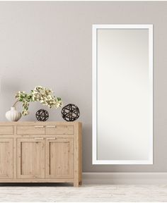 a white vase with flowers sitting on top of a wooden dresser next to a mirror