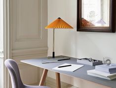 a desk with a lamp and some papers on it next to a framed picture in a room