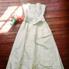 a white dress laying on top of a wooden floor next to a red flower bouquet