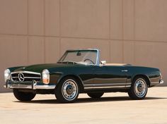 a green mercedes benz roadster convertible parked in front of a brown building with its top down