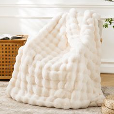 a white blanket sitting on top of a wooden floor next to a basket and plant