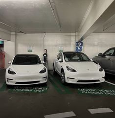 two electric vehicles are parked in a parking garage, one is white and the other is black