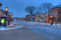 an empty street with snow on the ground and buildings in the background at night time