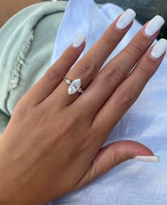 a woman's hand with white manicured nails and an engagement ring