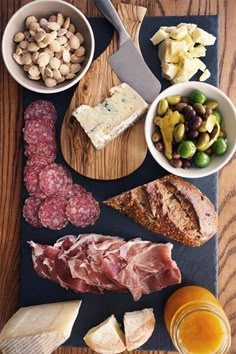 an assortment of meats and cheeses on a cutting board next to bowls of olives