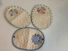 three handmade coasters are sitting on a table top, one has an applique and the other has a patchwork design