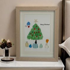 a christmas tree is displayed in a frame on a nightstand next to a vase with flowers