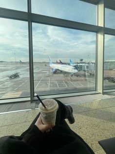 a person sitting in front of an airport window with a cup of coffee on their lap