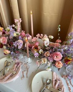 the table is set with pink and purple flowers, silverware, and napkins