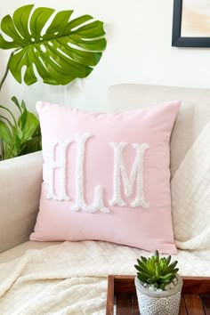 a pink pillow with the letter m on it sitting on a couch next to a potted plant