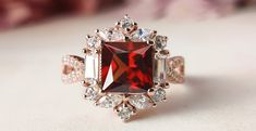 a fancy ring with a red stone surrounded by white and clear stones on a table