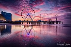 a ferris wheel sitting on top of a sandy beach next to the ocean at sunset