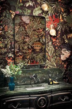 a bathroom sink sitting under a mirror in front of a floral wallpapered wall