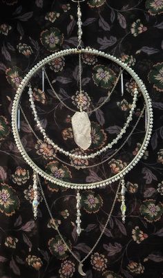 an assortment of necklaces hanging on a wall next to a flowered cloth background