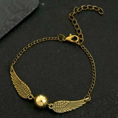 a gold bracelet with an angel wing charm and a golden ball on it's chain