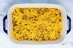 a casserole dish with cheese and ground beef in it on a marble counter top