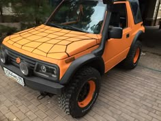 an orange and black truck parked on the side of a brick road in front of a building