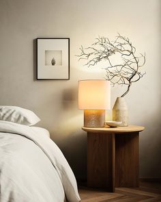 a bed with white sheets and pillows next to a table with a lamp on it