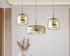 three lights hanging from the ceiling above a table with two vases and flowers on it