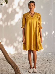 VALUES Handcrafted Organic Fair Minimal Waste CURATOR'S NOTE Crafted from soft mulmul cotton, this mustard yellow dress comes with smocking details at the hem and at the front and back yoke. It's finished with puff sleeves, side seam pockets and it is fully lined. THE DESIGNER STORY KHARA KAPAS, meaning 'pure cotton' in Hindi, started with the belief that design is a form of expression. True to its name, the brand continuously strives to achieve purity through their fabrics, designs and ethical Yellow Relaxed Fit Cotton Dress, Yellow Summer Dresses With Gathered Sleeves, Summer Yellow Dresses With Gathered Sleeves, Yellow Cotton Dress Relaxed Fit, Yellow Cotton Dress With Relaxed Fit, Yellow V-neck Relaxed Fit Dress, Yellow Relaxed Fit V-neck Dress, Yellow Smocked Bodice Midi Dress, Yellow Midi Dress With Smocked Bodice