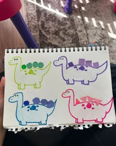 a person holding up a notebook with drawings of different dinosaurs on it's cover