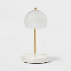 a white table lamp with a gold base on a white surface, against a plain background