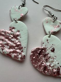 two heart shaped earrings with pink and white paint on them, hanging from silver earwires