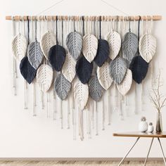 a wall hanging made out of leaves on a white wall next to a wooden table