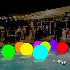 a group of people standing around a pool at night with colorful balls in the water