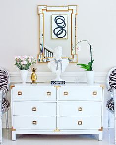 a white dresser topped with zebra print chairs next to a mirror and vase filled with flowers