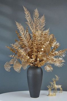 a vase filled with gold leaves on top of a white table next to a deer figurine