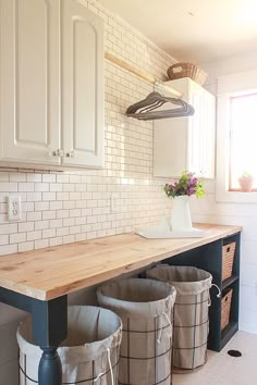 three buckets sitting on top of a wooden counter in a kitchen next to white cabinets