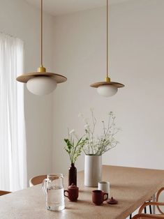 two pendant lights hanging over a table with vases and cups on top of it