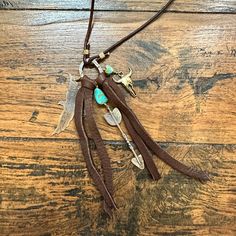 a necklace with feathers and turquoise stones on it sitting on a wooden table next to a cell phone