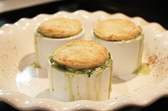 three small cakes in a white dish on top of a stove burner with green sauce