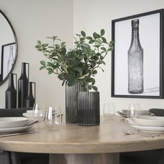 a dining room table with plates, glasses and vases on the table in front of it