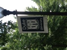 a lamp post with a duke banner hanging from it's side in front of trees