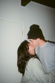 a man and woman kissing each other in front of a white wall with a door