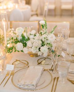 the table is set with white flowers and gold place settings for an elegant wedding reception