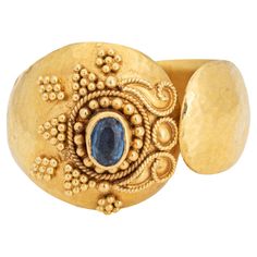 Stylish vintage sapphire ring crafted in 22 karat yellow gold. Small blue sapphire measures 4mm x 3mm. The sapphire is in very good condition and free of cracks or chips. The distinct hand-made ring in bright buttery 22k yellow gold features fine granulation work in a star like pattern and scrolled wire work. Hand hammered details adorn the wide (15.5mm - 0.61 inches) cigar style band. The ring is great worn alone or stacked and makes a nice statement on the hand. The low rise ring (6.5mm - 0.25 Gold Oval Yellow Sapphire Ring, Oval Yellow Sapphire Ring In Gold, Formal Gold Ring With Yellow Sapphire, Formal Gold Sapphire Ring With Yellow Sapphire, Gold Sapphire Ring With Gemstone, Gold Round Yellow Sapphire Ring, Gold Hand Forged Sapphire Ring, Gold Yellow Sapphire Ring, Round, Gold Yellow Sapphire Round Ring