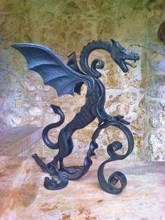 a black metal dragon statue sitting on top of a stone floor next to a wall