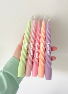 a hand holding five candles with different colors and sizes in each candle, all lined up together