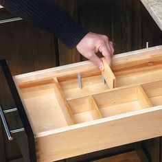 a person holding a piece of wood in their hand over an open drawer with drawers on both sides