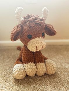 a brown and white crocheted cow sitting on the floor with its eyes closed