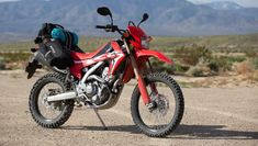 a red motorcycle parked on top of a dirt road