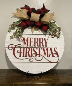 a merry christmas sign on top of a wooden table with red and green bows hanging from it