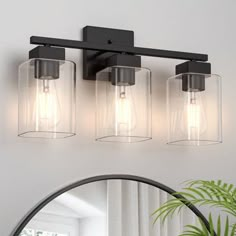 three light bathroom fixture with clear glass shades and black metal frame, on a white wall