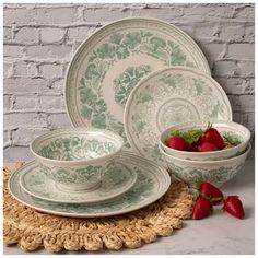 a table setting with strawberries on the placemat and white brick wall behind it