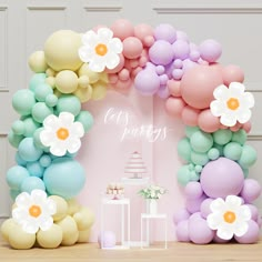 an arch made out of balloons with flowers on the top and bottom is decorated in pastel colors