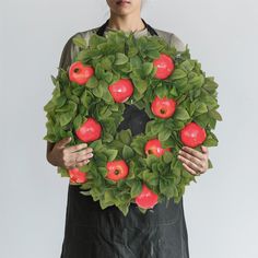 a woman holding up a wreath made out of apples and leaves with an apple on top